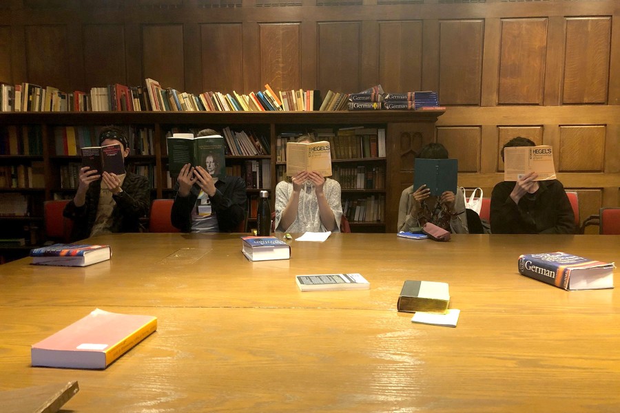 Five students in classroom with books open covering their faces