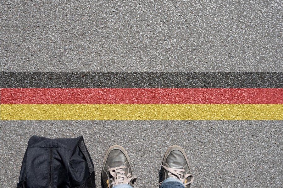 Pavement view of German stripes infront of a backpack and someone's sneakers