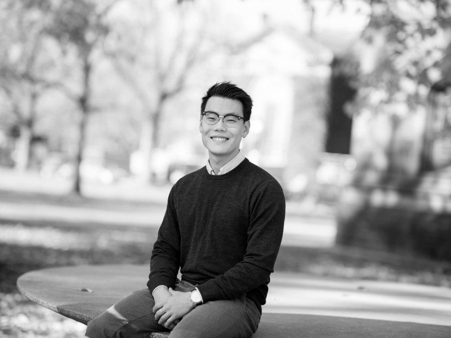 Smiling grad student sitting on an art sculture with campus in background