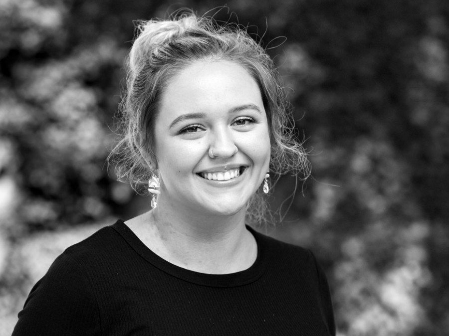 Undergraduate Student smiling with blurred shrubs in background