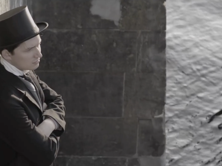 Man wearing top hat leaning against wall with water reflecting in background