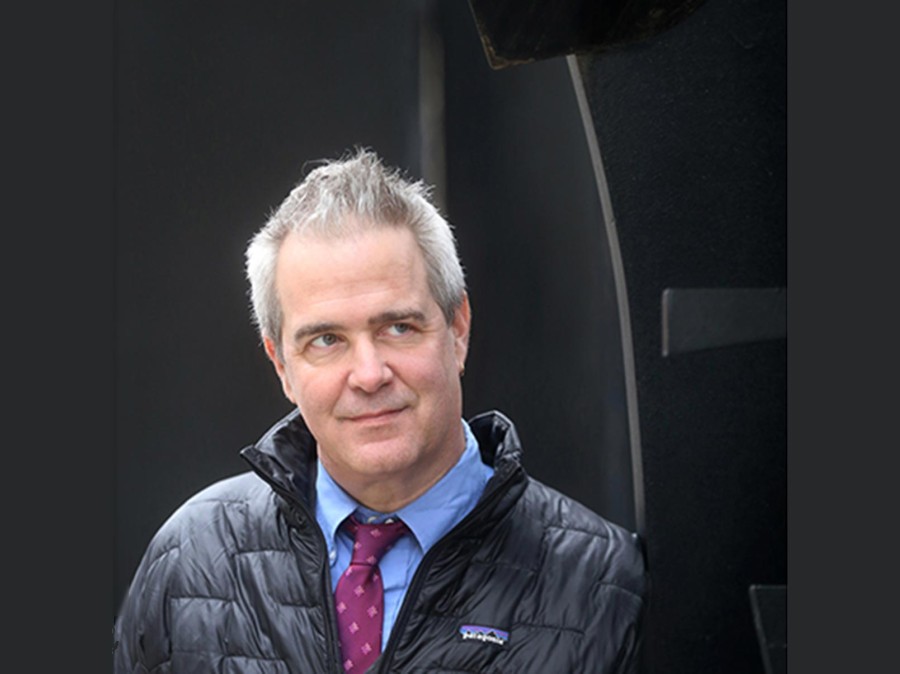 Man wearing outer coat and a tie, looking up to his left.