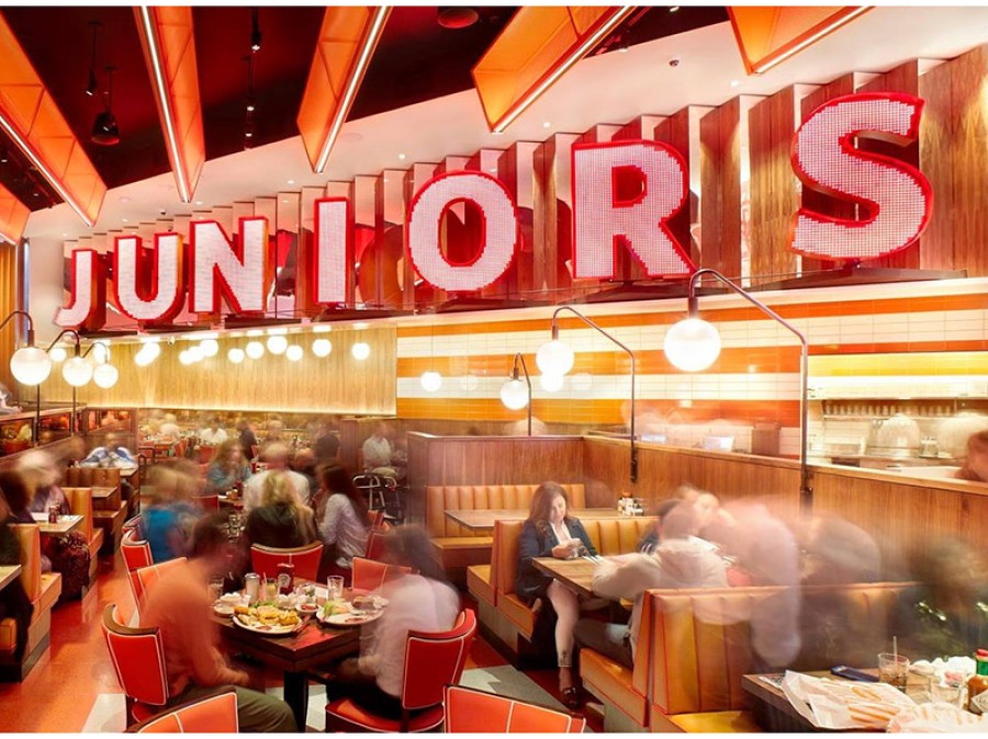 Long exposure image of patrons in a diner with JUNIORS as signage above in colorful lighting