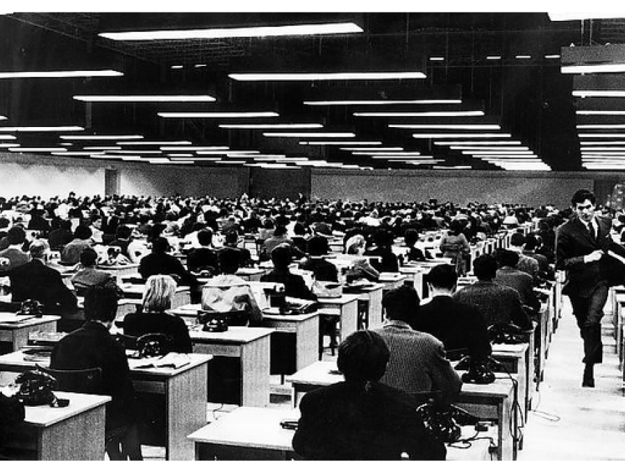 Person walking toward camera with rows and rows of office workers at desks