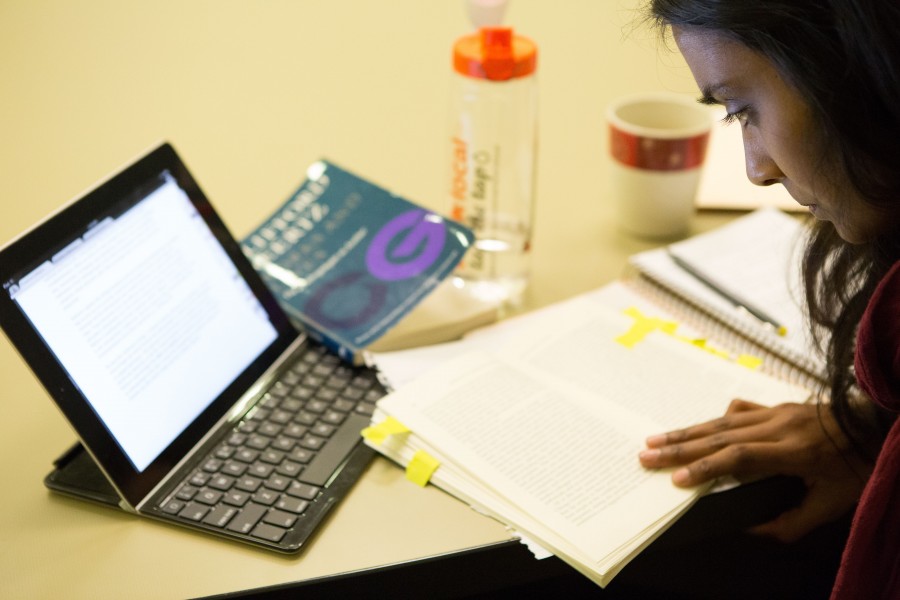 Student reading pages with open computer device on desk.