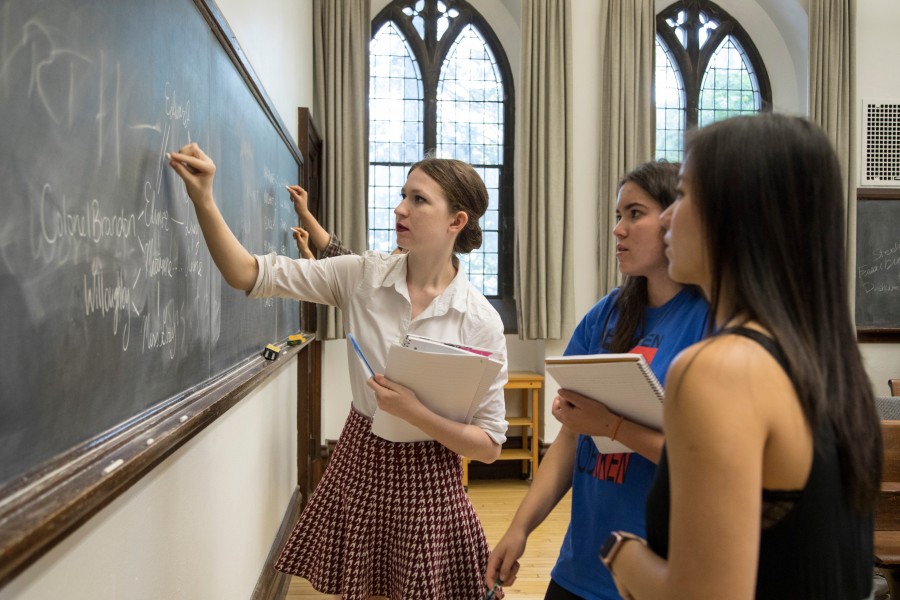 Students writing on chalkboard at front of University classroom.