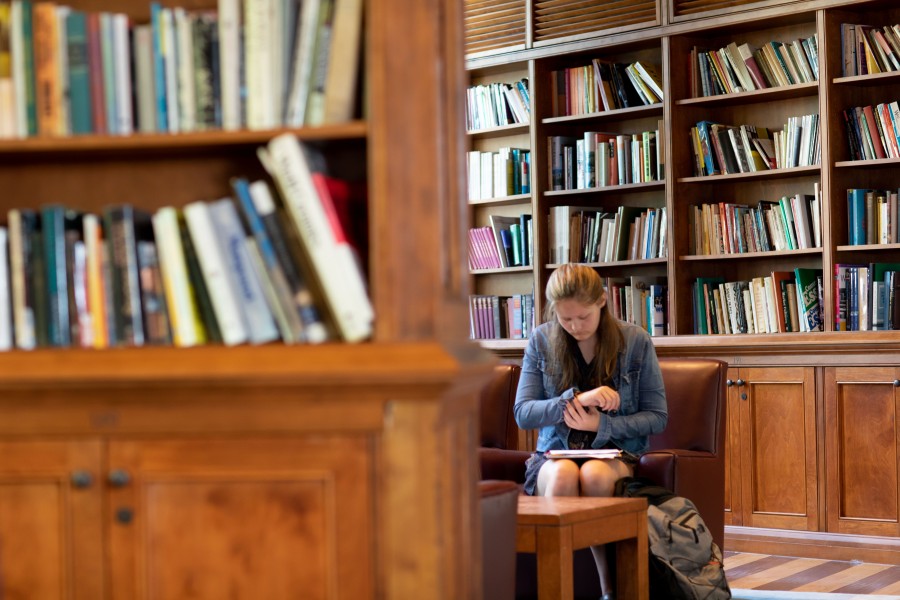 Student reading in library, surrounded by book shelves.