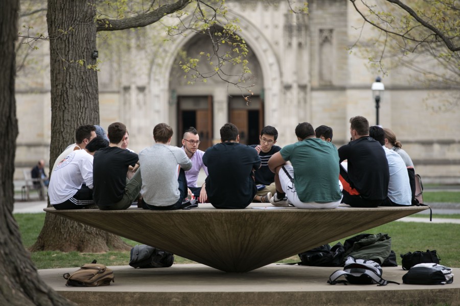 Students sitting on modern artwork sculture in a circle with Chapel in background.